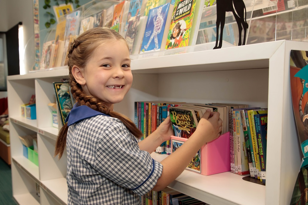 A young student is taking a book from a shelf in the library.
