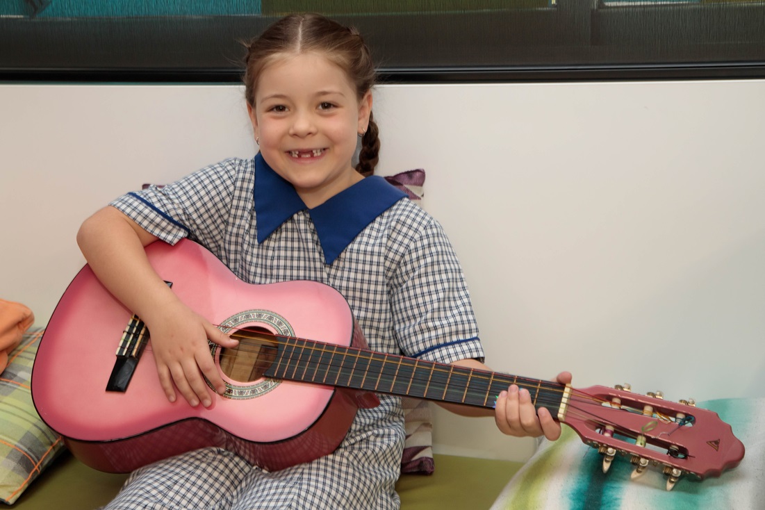 A young student sitting on a couch, holding a guitar.