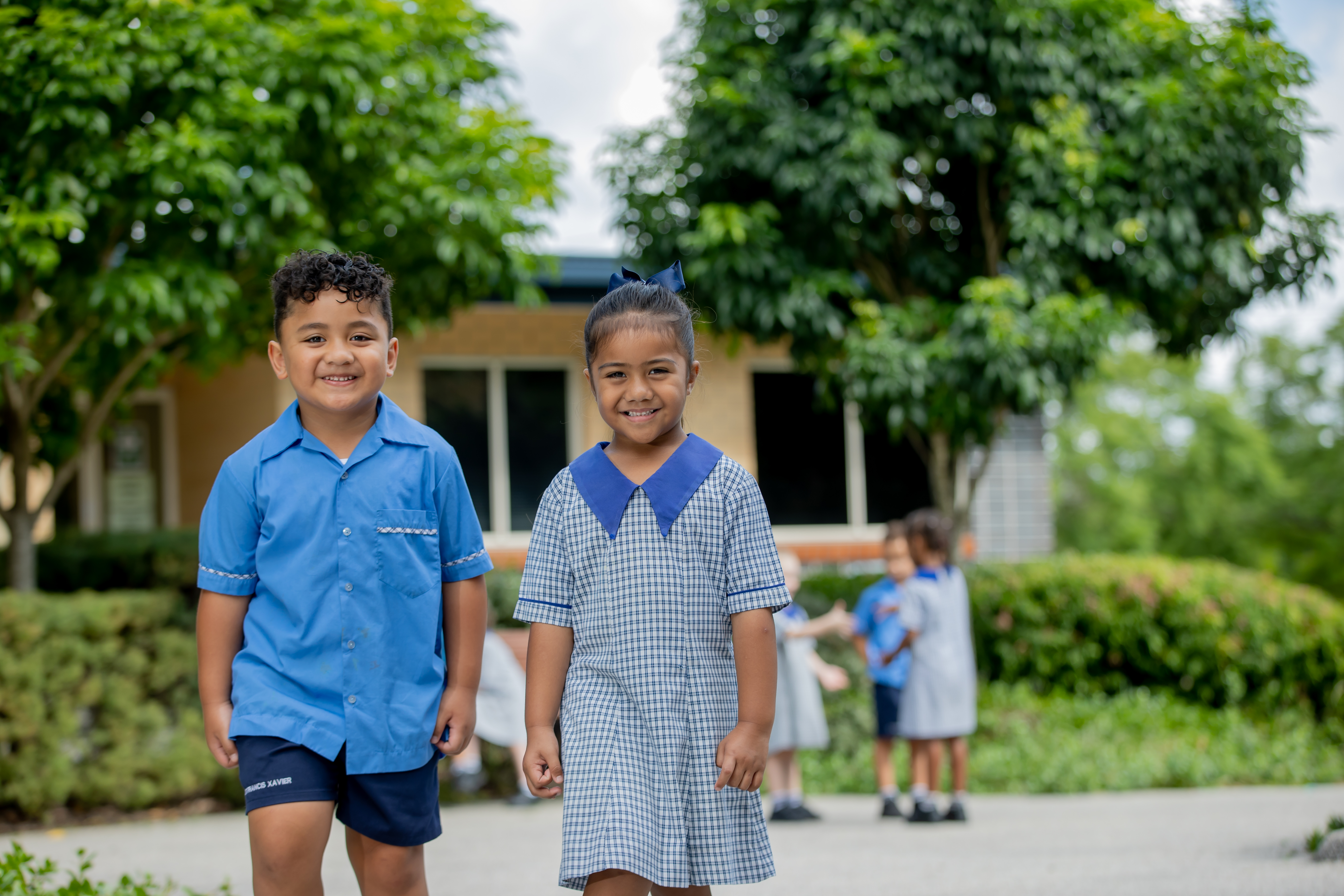 Two students are walking in the school grounds. There is a group of three students in the background behind them.