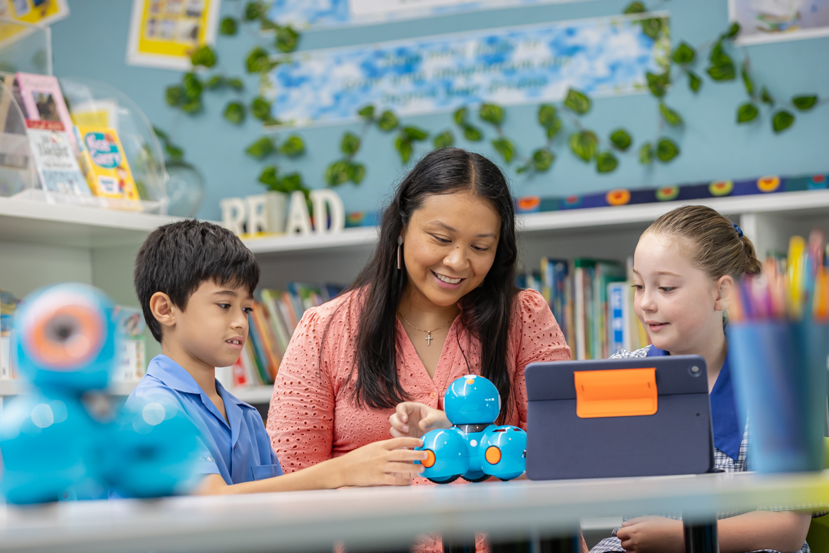 Two students are sitting at a desk with a teacher.
