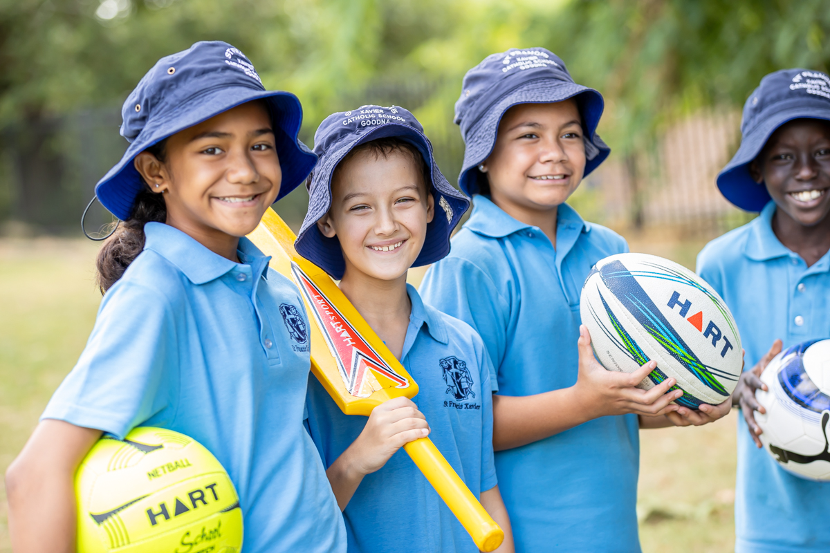 Four students in sport uniforms. They are holding balls and a bat.